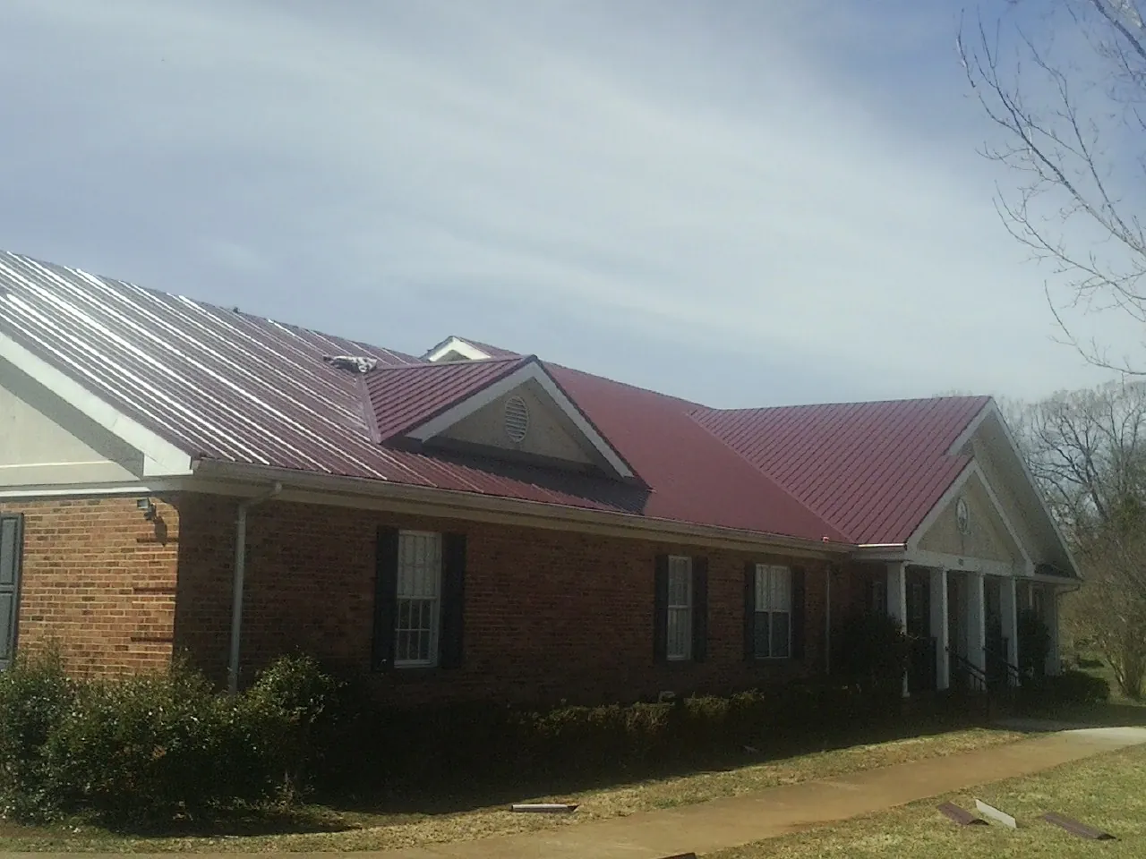 Red metal roof with gabled entries on a long brick building, from a Hail Damage Roof Repair job in Harrisville