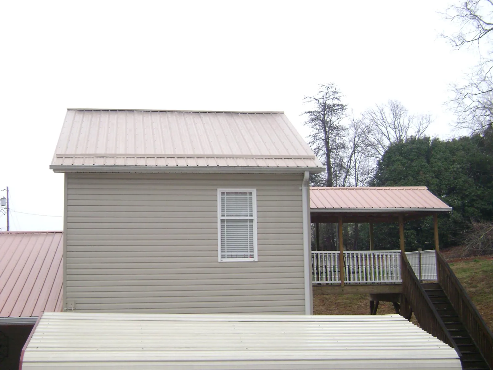 Tan metal roofs on a two story addition and attached porch, from a Roof Replacement job in Harrisville
